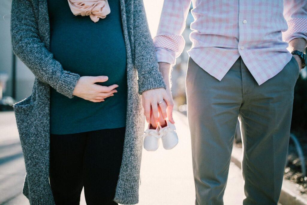 man standing beside pregnant woman holding baby's shoes during daytime